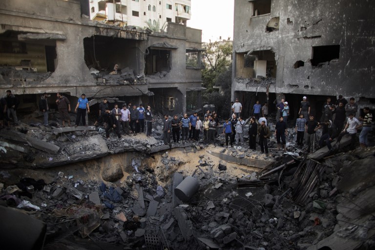 AFTERMATH. Palestinian men gather around a crater caused by an Israeli air strike on the al-Dallu family's home in Gaza City on November 18, 2012. AFP PHOTO/MARCO LONGARI