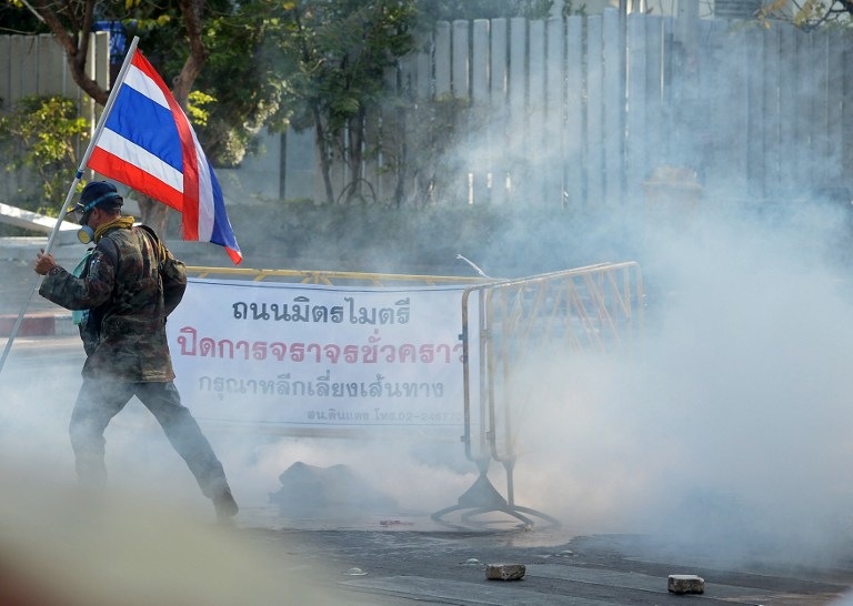GASSED. A Thai anti government protester holds a national flag during a rally at a stadium to register party-list candidates in Bangkok on December 26, 2013. AFP / Pornchai Kittiwongsakul