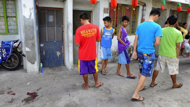 Residents walk past by a door with lighted candles (L) and blood stains (bottom L) after a gunman reportedly shot a mother and child during a rampage in Kawit, about 40 kms (25 miles) south of Manila on January 4, 2013. AFP PHOTO / JAY DIRECTO