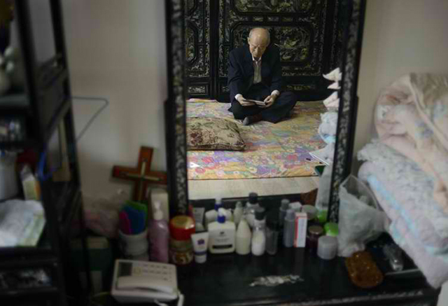 Kim Se-Rin is reflected in a mirror as he sits on his bed looking at photos of his South Korean family, prepared ahead of a meeting with relatives in the North. Among tens of thousands of wait-listed applicants, the 85-year-old is one of just 82 South Koreans who participated in the meeting beginning February 20. Photo by Ed Jones/AFP