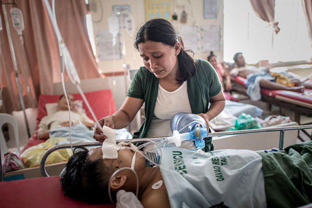 HUSBAND AND WIFE. Jennifer Purga checks on her husband and pumps air into his lungs in a Tacloban hospital, after a leg amputation led to an infection. Photo by Philippe Lopez/AFP