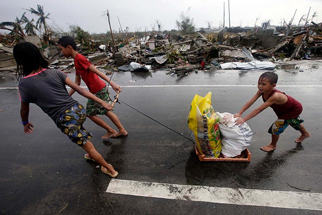 STRUGGLING. Children pull sacks of goods they recovered from abandoned stores as they go past the rubble of houses in Tacloban City. Photo by Dennis Sabangan/EPA